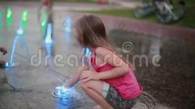 在<strong>炎热</strong>的<strong>夏天</strong>，可爱的小女孩蹲在喷泉边玩彩色喷水。